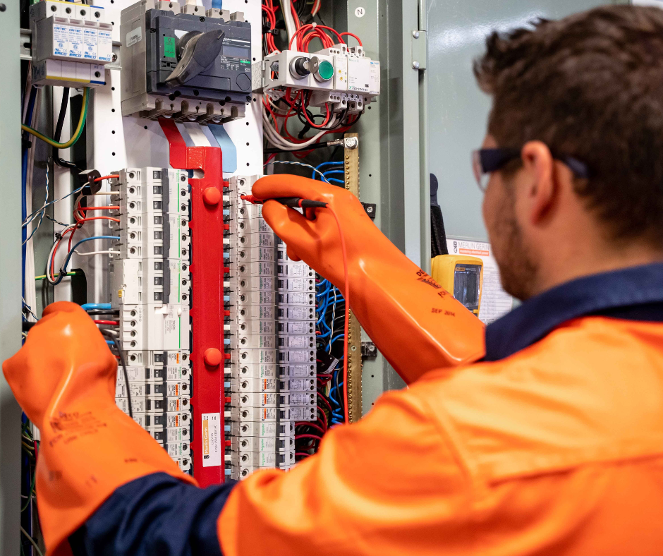 Personne de dos travaillant sur un panneau électrique en portant des gants.